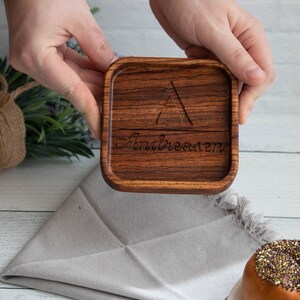 May include: A square wooden coaster with a triangle design and the name "Andreason" engraved on it.