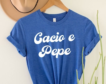 Könnte beinhalten: Ein blaues T-Shirt mit dem Text "Cacio e Pepe" in weißen Retro-Lettern.