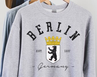 May include: Gray sweatshirt with a black and white graphic of the Berlin coat of arms. The graphic includes a bear, a crown, and the text "BERLIN EST. 1237 -Germany-"