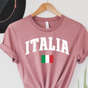Pu&ograve; includere: Una maglietta color rosa polvere con la scritta "ITALIA" in bianco e la bandiera italiana stampata sulla maglietta.