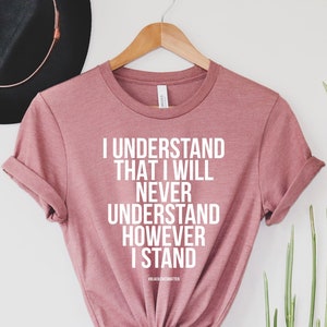 K&ouml;nnte beinhalten: Ein staubiges rosafarbenes T-Shirt mit dem Text "I understand that I will never understand however I stand" in wei&szlig; gedruckt.