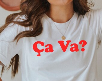 Op de afbeelding: Wit T-shirt met de tekst "Ca Va?" in rode letters.