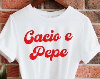 Könnte beinhalten: Weißes T-Shirt mit dem Text "Cacio e Pepe" in roten Kursivbuchstaben.