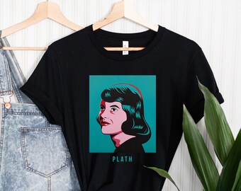 May include: Black t-shirt with a graphic of Sylvia Plath's face in a teal blue square with the word "PLATH" underneath.