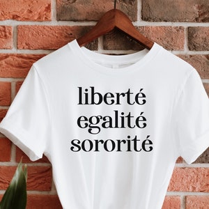 Puede incluir: Camiseta blanca con el texto "liberté égalité sororité" impreso en negro.