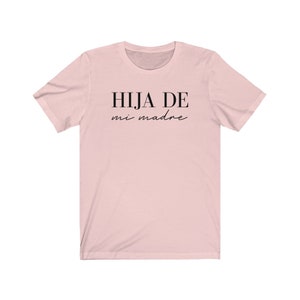 May include: A pink t-shirt with the text "HIJA DE mi madre" in black.