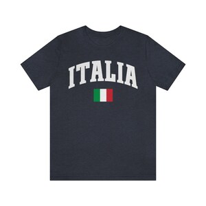 Pu&ograve; includere: Una maglietta blu navy con la scritta "ITALIA" in bianco in un font ad arco. La bandiera italiana &egrave; sotto il testo.