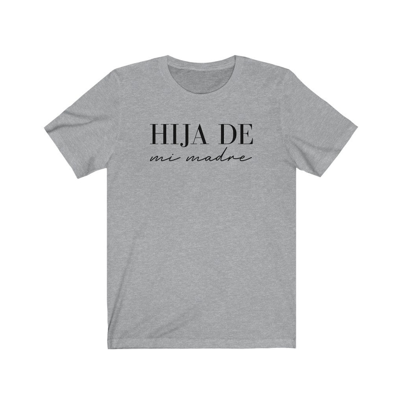 May include: A heather grey t-shirt with the text "HIJA DE mi madre" in black.
