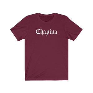 May include: A maroon short-sleeved t-shirt with the word "Chapina" printed in white in a gothic font.