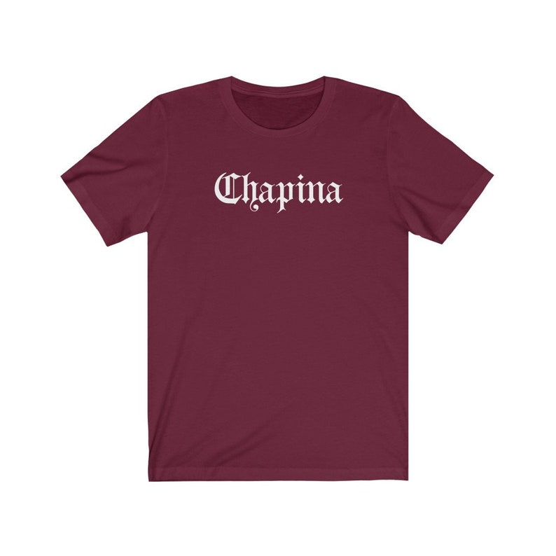 May include: A maroon short-sleeved t-shirt with the word "Chapina" printed in white in a gothic font.