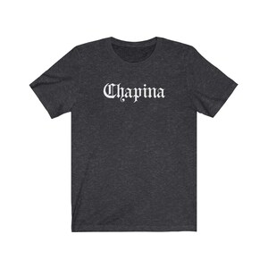 May include: A dark heather grey t-shirt with the word "Chapina" printed in white in a gothic font.