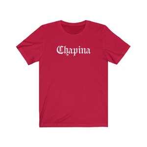 May include: Red short-sleeved t-shirt with the word "Chapina" printed in white in a gothic font.