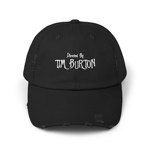 May include: Black distressed baseball cap with white embroidered text that reads "Directed By TIM BURTON".