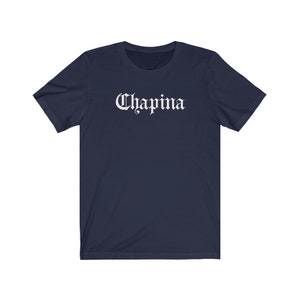 May include: A navy blue t-shirt with the word "Chapina" printed in white in a gothic font.