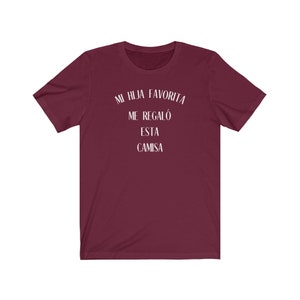 May include: Burgundy t-shirt with white text that reads "Mi hija favorita me regal&oacute; esta camisa".