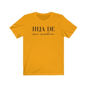 May include: A yellow t-shirt with black text that reads "HIJA DE mi madre".
