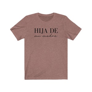 May include: A heather brown t-shirt with the text "HIJA DE mi madre" in black.