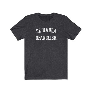 May include: Dark heather grey t-shirt with white text that reads "Se Habla Spanglish".