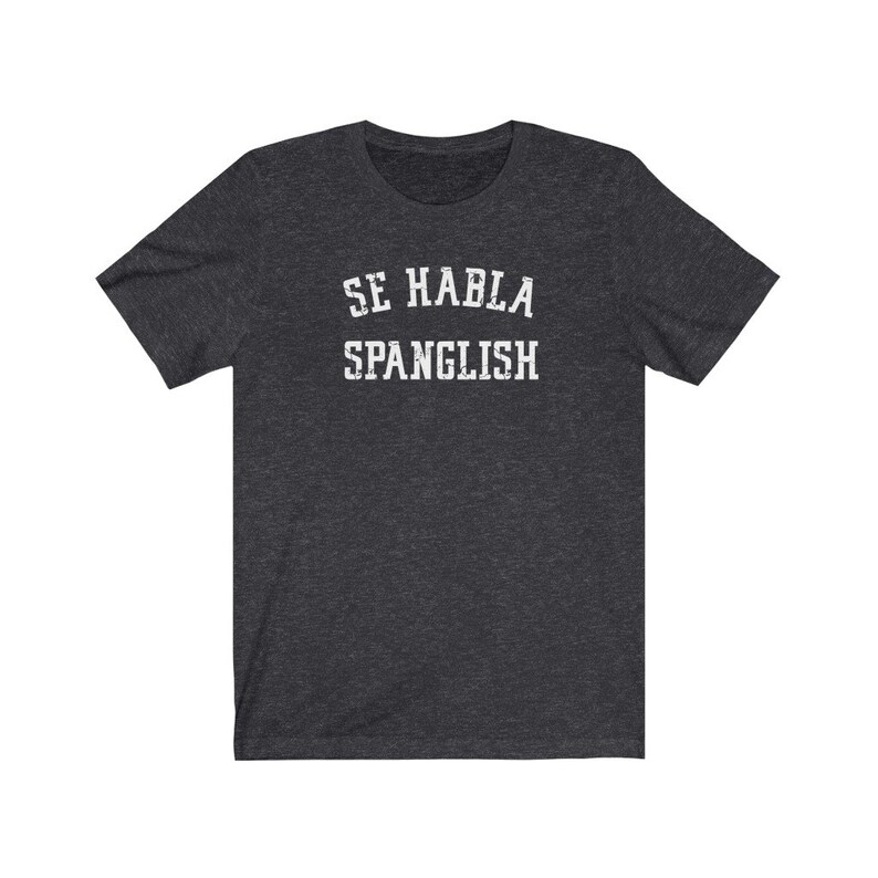 May include: Dark heather grey t-shirt with white text that reads "Se Habla Spanglish".