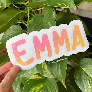 May include: A die-cut sticker featuring the name EMMA in a bold, sans-serif font. The letters display a vibrant gradient transitioning from pink at the top to orange at the bottom. The sticker has a white border and includes the text Pink Lemonade.