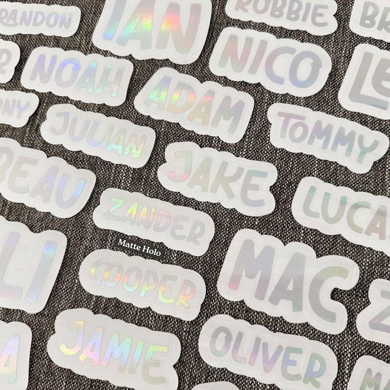 May include: A collection of die-cut stickers featuring various names such as Ian, Noah, Adam, Nico, Tommy, Julian, Jake, Beau, Zander, Lucas, Cooper, Mac, Jamie, and Oliver. Each sticker has a matte holographic finish with white borders.