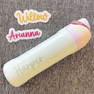 May include: A pale green Owala water bottle with the name Harper printed in a script font on the side. Two separate white stickers are included, one with the name Willow in yellow script and one with the name Arianna in pink script lettering.