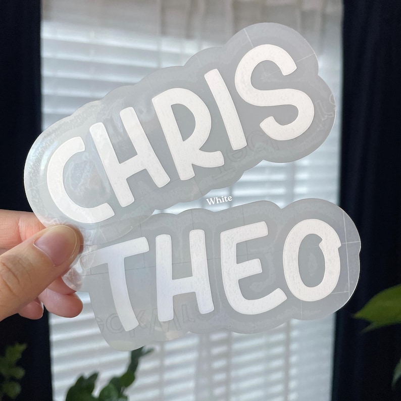 May include: A clear adhesive decal featuring the white text CHRIS and THEO in a bold, rounded sans-serif font. The names are arranged on two separate lines with a contoured, transparent border following the shape of the letters.