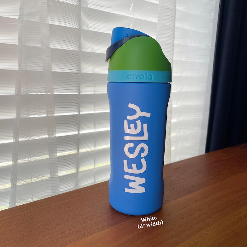May include: A blue Owala water bottle with a green and blue lid. The name WESLEY is printed in white vertical lettering on the side. The text at the bottom indicates a white color and a 4 inch width for the lettering on this reusable bottle.