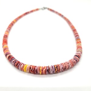 May include: A colorful necklace made of flat, round shell beads. The beads are in shades of red, orange, yellow, and purple. The necklace has a silver-colored clasp and is displayed against a white background.