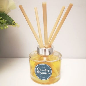 May include: A clear glass diffuser bottle with a silver lid and natural reed sticks. The bottle contains a yellow liquid and has a label that reads "Candles Boutique by Donna Bora Bora".