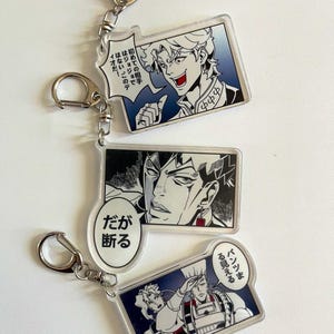 May include: Three clear acrylic keychains with manga-style illustrations and silver-coloured metal clasps. Each keychain features a different character with speech bubbles containing Japanese text. The keychains are rectangular and oval-shaped.