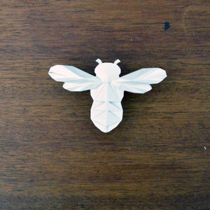 Peut inclure: Abeille en origami blanche sur une surface en bois brun foncé.