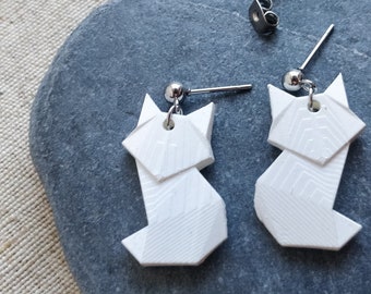 Può includere: Un paio di orecchini a forma di gatto origami bianchi con ganci per orecchini argentati. Gli orecchini sono su uno sfondo di pietra grigia.