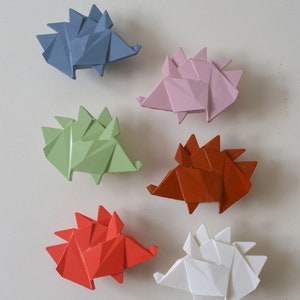 Könnte beinhalten: Sechs Origami-Igel in verschiedenen Farben: blau, rosa, grün, orange, rot und weiß. Die Igel sind aus Papier und haben ein stacheliges Design.