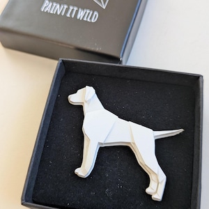 Puede incluir: Una figura de perro geométrico blanco dentro de una caja negra con interior negro. La caja está abierta, revelando el objeto en forma de perro. La tapa de la caja es visible, con el texto "PAINT IT WILD" en blanco.