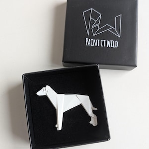 Könnte beinhalten: Ein weißer, geometrischer Hunde-Ansteckpin in einer schwarzen Schachtel. Der Pin ist eine stilisierte Darstellung eines Hundes. Die Schachtel trägt den weißen Schriftzug "PAINT IT WILD". Der Pin befindet sich in einer schwarzen Schachtel.
