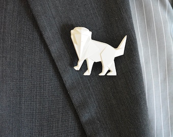 May include: A white origami animal brooch in the shape of a cat, pinned to a dark grey suit jacket.