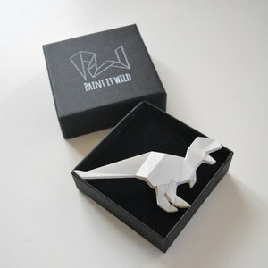 Könnte beinhalten: Eine weiße Origami-Dinosaurierfigur in einer schwarzen Box mit dem Text "PAINT IT WILD" auf dem Deckel.
