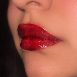 Pode incluir: Close-up dos l&aacute;bios de uma pessoa usando um batom vermelho escuro brilhante.