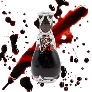 Può includere: Flacone di profumo decorativo con un design a filigrana argentata e una parte superiore trasparente e appuntita. La bottiglia è riempita con un liquido scuro ed è posta su uno sfondo bianco con schizzi rossi.