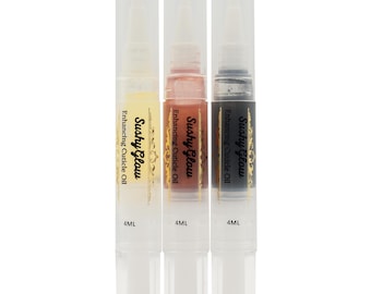 Puede incluir: Tres bolígrafos de aceite para cutículas de plástico transparente con puntas de pincel, cada uno con 4 ml de líquido. Las etiquetas dicen Sushy Glow Enhancing Cuticle Oil en negro. Los aceites son amarillo, rosa claro y gris oscuro.