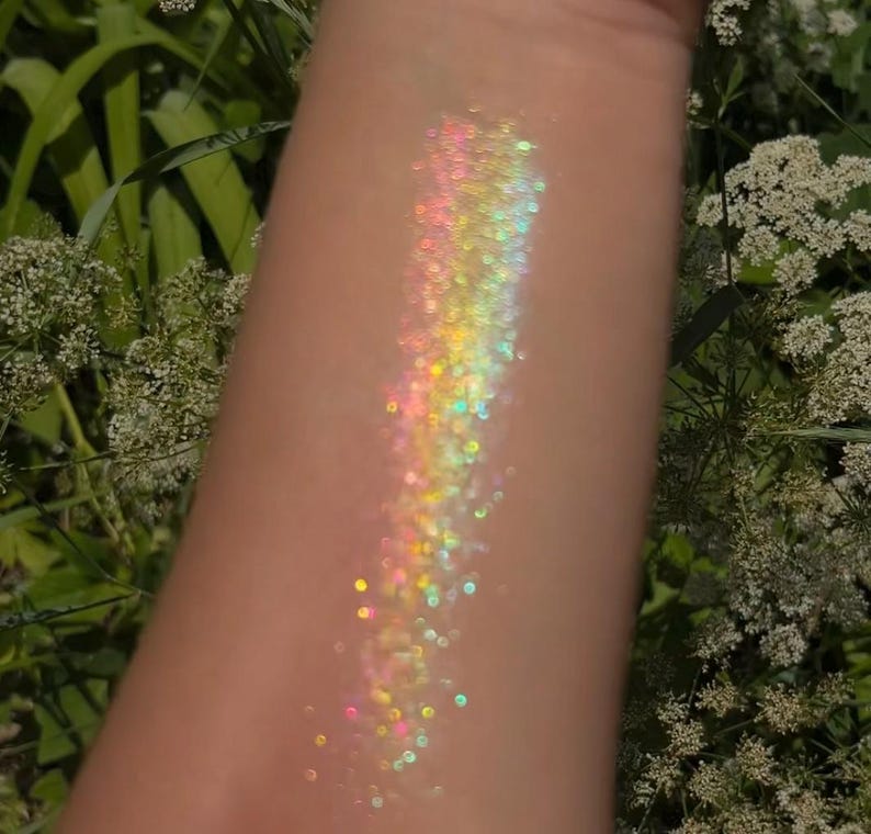May include: A close-up of iridescent glitter on skin, showing a rainbow of colors, including pink, yellow, green, and blue.