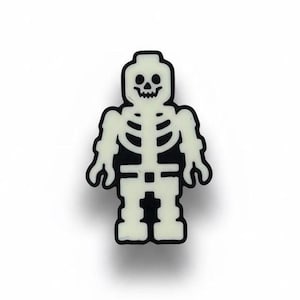 May include: A black and white skeleton-shaped charm. The skeleton has a white, glowing appearance with a black outline. The charm is a Halloween-themed accessory.