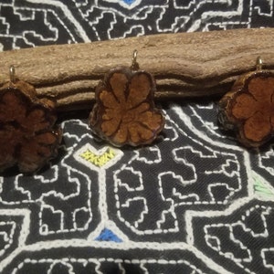 May include: Three brown wooden flower-shaped pendants with gold-colored metal loops. The pendants are on a brown wooden branch.