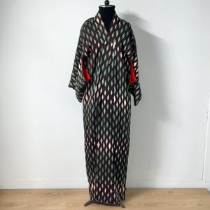May include: A full-length kimono with a diamond pattern in shades of brown, green, and white. The kimono has long sleeves with red accents at the cuffs. It is displayed on a black mannequin head and stand.