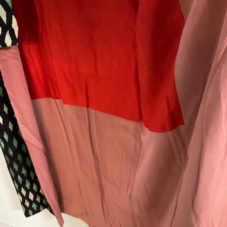 May include: A multi-colored garment featuring a patchwork design. The top section is a vibrant red, transitioning to a muted rose and then a soft pink. A section with a black and green diamond pattern is visible.