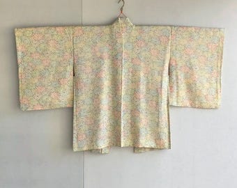 Könnte beinhalten: Ein Vintage-Kimono mit floralem Muster in Pastellfarben wie Rosa, Blau und Gelb. Der Kimono hängt an einem Kleiderbügel vor einem neutralen Hintergrund. Die Ärmel sind weit und der Stoff wirkt leicht. Der Kimono ist ca. 150 cm breit.