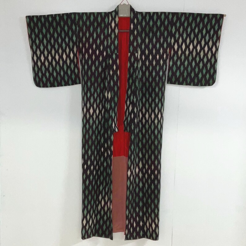May include: A vintage kimono with a diamond pattern in black, green, and white. The interior lining is red and pink. The kimono is hanging on a hanger against a white background.