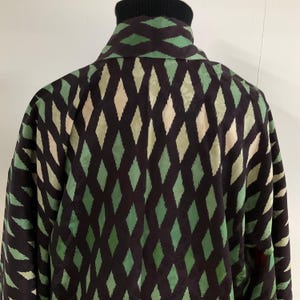 May include: A dark brown jacket with a repeating diamond pattern in shades of green and beige. The jacket has a black turtleneck collar and a collared neckline. The sleeves are visible on the sides.