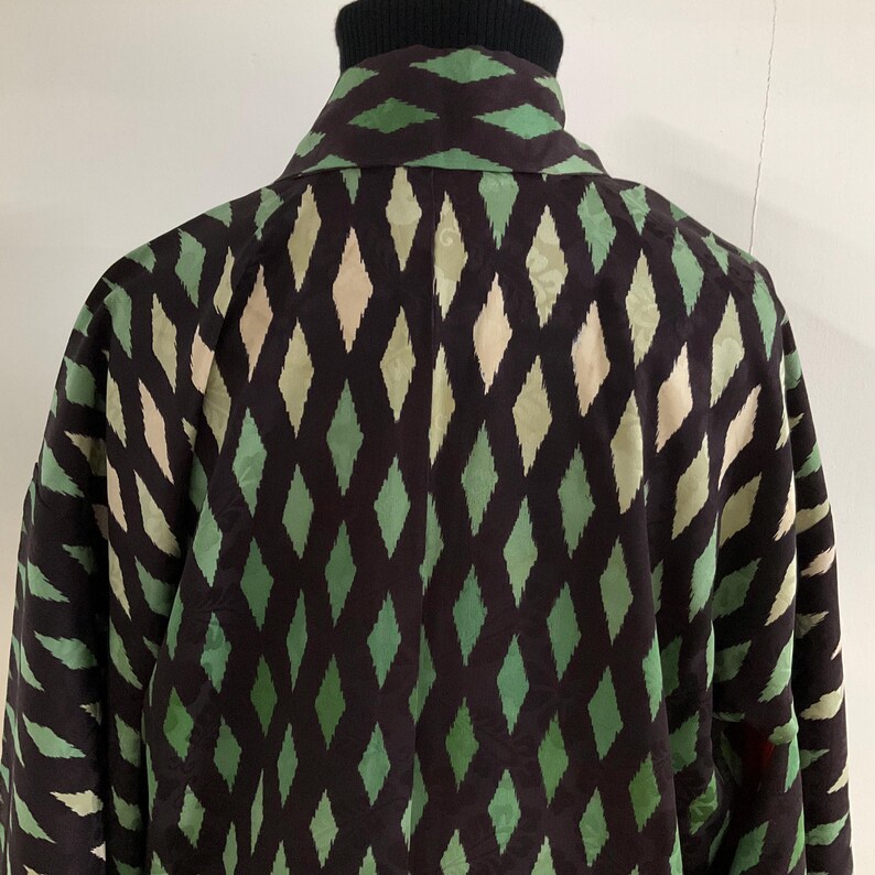 May include: A dark brown jacket with a repeating diamond pattern in shades of green and beige. The jacket has a black turtleneck collar and a collared neckline. The sleeves are visible on the sides.